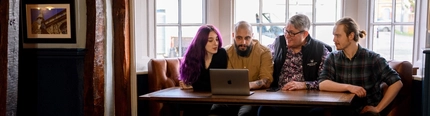 Three Men and a Woman sat at a table looking at the laptop in front of them.