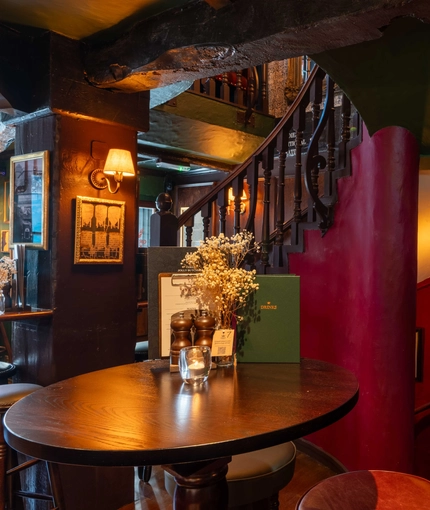 The interior restaurant and seating area focusing on a table positioned next to a set of stairs going up and down with a sign that says 'Down to gents' and points down the stairs at the Three jolly Butchers.