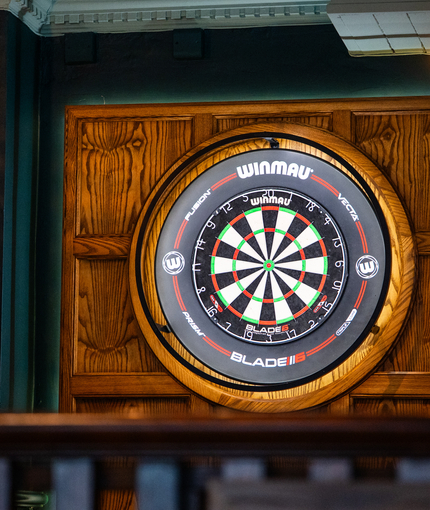 A close up view of an illuminated dartboard on a wood panelled wall inside the Scholars Arms.