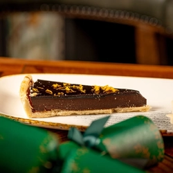 A festive wooden table holding a plated Chocolate and Orange Tart.