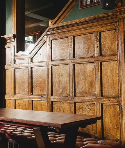 A wood panelled interior restaurant seating area at the Masons Arms, with upholstered bar stools and bench, and grape vines carved into the coving.