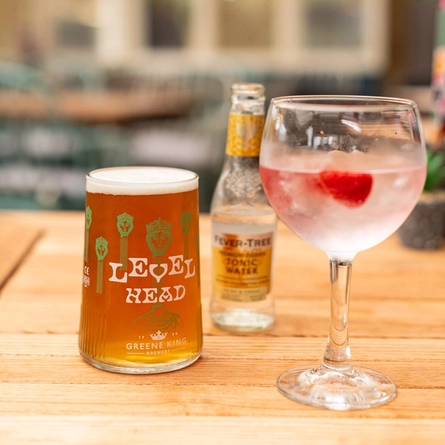 A glass of Level Head ale, a cocktail in a glass and a bottle of Fever Tree tonic water, sitting on a wooden table.
