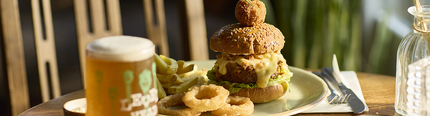 An advertising image of a plated signature burger sat on an interior table with a pint of Level Head at a Chef & Brewer venue.