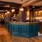 The wood panelled bar, and interior restaurant seating area of The Hollybush in Lichfield, with a fireplace at the end of the room, and four spherical glass lights hanging above the counter.