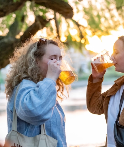 An image focusing on 2 friends stood within the beer garden area by the waterside enjoying drinks during The Boat Race event at The Crabtree.