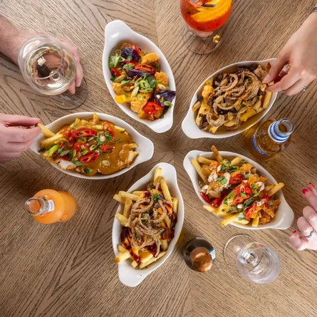 Small plates of loaded fries with hands in the image