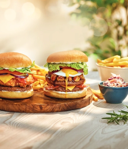 A board of 2 burgers with a side of fries and coleslaw