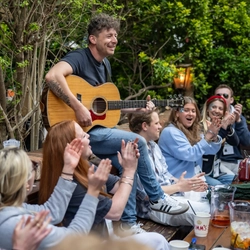 An image of customers sat at a table outside with drinks enjoying live music during the Boat race event at The Crabtree.
