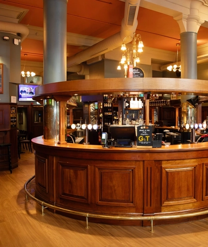 The wood panelled interior restaurant seating area and U-shaped bar at the Rhoderick Dhu in Glasgow; with upholstered booth seating, and TVs on the walls.