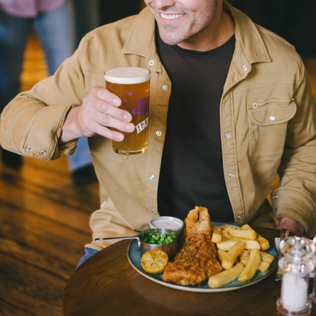 An image of a person enjoy a Fish & Chips dish with a pint of Hazy Day sat within the interior restaurant seating area at an Urban Core Venue.
