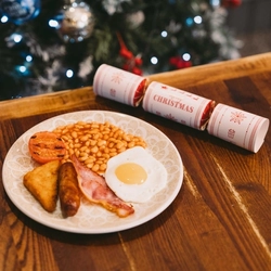 A childrens cooked breakfast on a table against a festive background.   There is a Christmas cracker on the table.