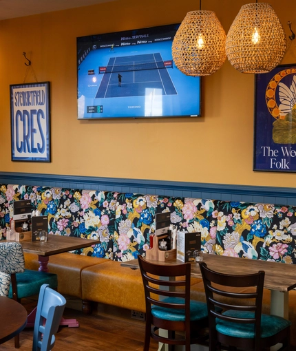 An interior restaurant seating area at The Kittoch, with a long upholstered booth seat, and a TV on the wall.