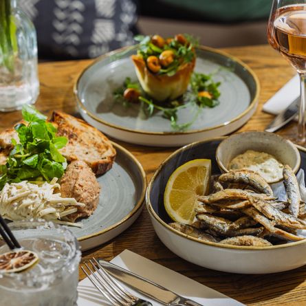 An advertising image showing a selection of starter dishes from the Prix Fixe menu sat on a table within the interior restaurant seating area at The Four Oaks.