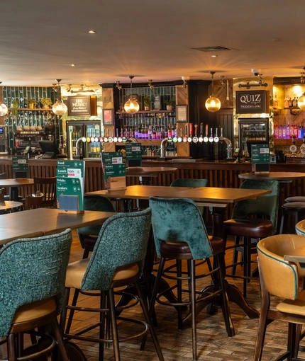 The bar and interior restaurant seating area of the Rudds Arms; with upholstered bar stool seating, and spherical lights above the bar.