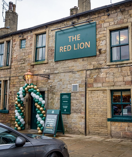 The exterior facade and signage of The Red Lion in Skipton, with a balloon arch around the front door.
