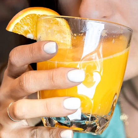 A glass of orange juice, being sipped by a woman.