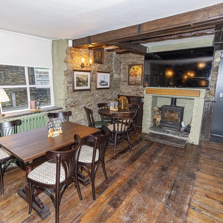 The interior seating area with wooden tables, exposed brickwork walls, log burner fireplace, large wall mounted TV screen at The Flag Inn.
