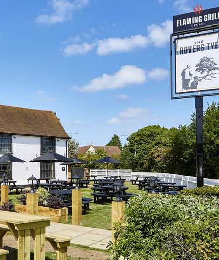 The exterior facade with signage and beer garden seating area of the Rovers Tye.