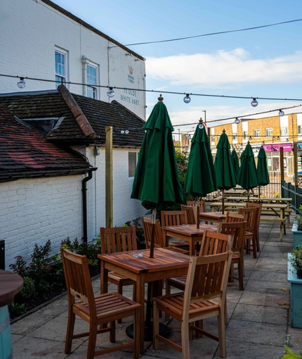 The exterior facade and beer garden seating area of The White Hart, with wooden picnic tables and shade umbrellas.
