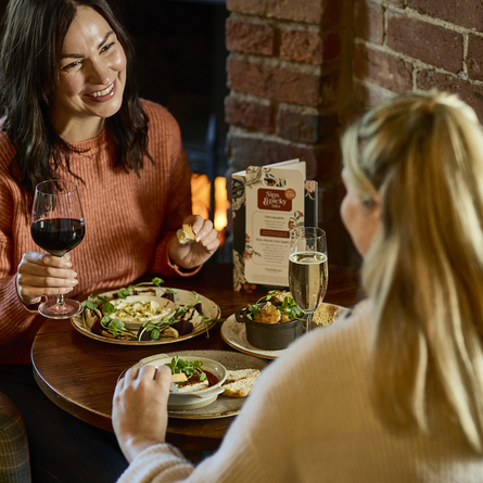An image of 2 customers sat within the interior restaurant and seating area enjoying a selection of picky bits and drinks available at Chef & Brewer venues.