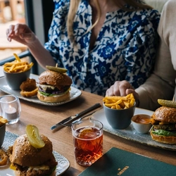 A close up image of a group of people sat at a table within the interior restaurant seating area enjoying a selection of drinks and Burger dishes at a Heritage venue.