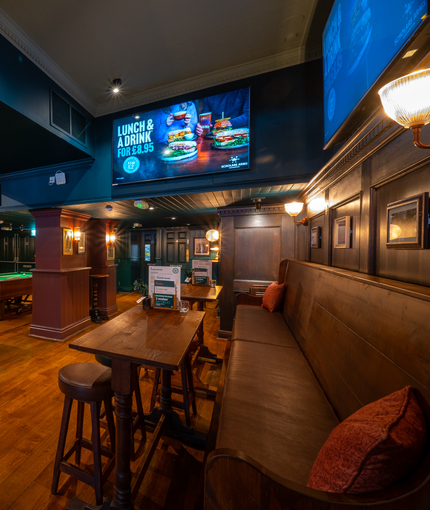 An interior restaurant seating area at the Scholars Arms; with TVs on the walls, padded bench seating, and two pool tables.