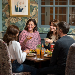 A group of people sitting around a table smiling and having a meal, with drinks in their hands.
