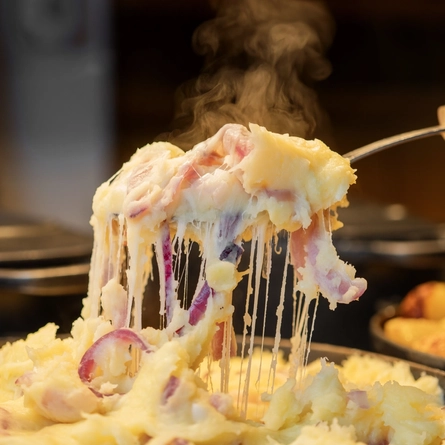 A close up view of a large spoonful of cheesy onion mashed potato being lifted out of a large roasting dish.