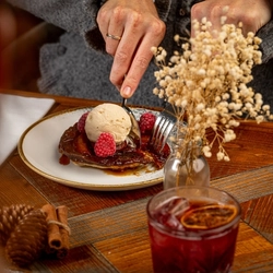 A close-up of a dessert plate  topped with a scoop of vanilla ice cream. A hand is holding a spoon, ready to take a bite.