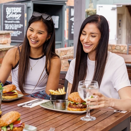 An exterior shot of people enjoying drinks and burgers within the beer garden seating area at a Community Pub with Food venue.