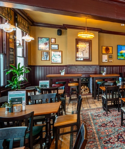 The interior restaurant seating area of The Fountains Abbey, with wooden tables and chairs, a fireplace, and two TVs on the walls.