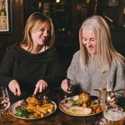 A lifestyle image focusing on 3 customers sat at a table enjoying Mothers Day main dishes and drinks within the interior restaurant seating area at a Heritage venue.