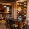 An interior restaurant seating area at the Ye Olde Leathern Bottel in Barkham, with stone flooring, wooden beams, a brick wall with a fireplace, and bottles of wine in a glass display case in another wall.