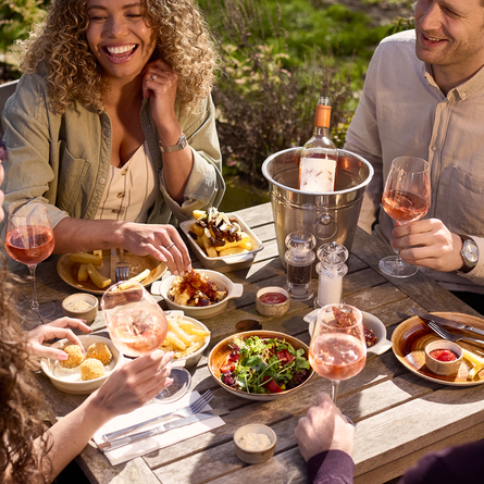 An image of 4 friends sat at a table within the exterior beer garden enjoying glasses of rose wine and a selection of picky bits at a Chef & Brewer venue.