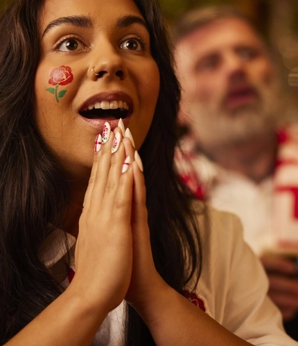 An image of a woman wearing a sport team shirt, watching a sporting event.