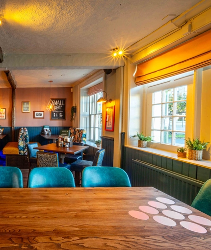 An interior restaurant seating area at The White Hart, with upholstered seats, and potted plants on the window sill.