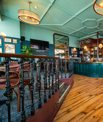 The bar area inside The Fountains Abbey, with wooden tables and chairs, a raised seating section with wooden railings, and a TV on the wall.