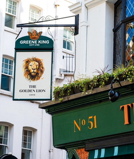 A close up view of the exterior pub sign on the exterior wall of The Golden Lion. The sign features the Greene King logo and an illustration of a lion's head above the words "The Golden Lion, Soho".