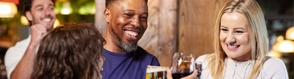 A mixed group of people inside a pub, smiling and clinking glasses in a Cheers motion.