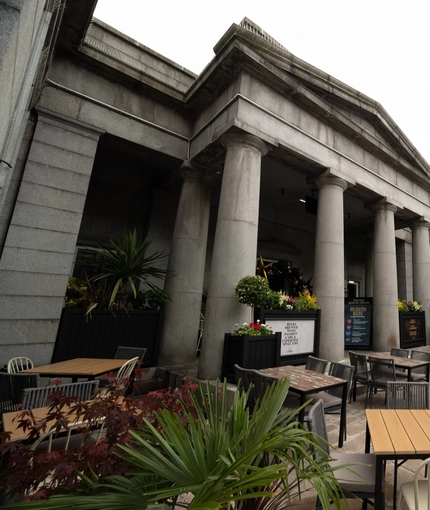The exterior facade, signage, and beer garden seating area at the Old School House in Aberdeen, with large stone pillars, planter boxes, wooden picnic tables, and shade umbrellas.