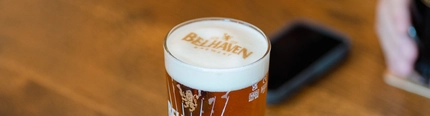 An image of a pint sat on an interior table with a detailed branded foam head design at The Belhaven Brewery.