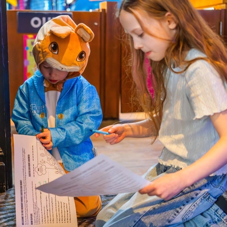 Two children, one dressed as OPeter Rabbit, holding activity pages.