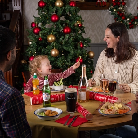A group of people and a child seated around a festive decorated table with plated meals in front of them.