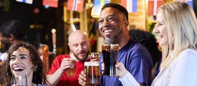 A mixed group pf people sitting at an indoor table reacting to a sporting event.