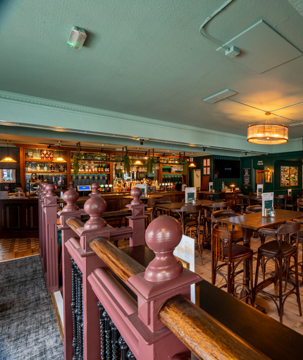 The interior restaurant seating area and bar at The Junction in Upminster, with TVs on the walls, bar stool seating, and an upholstered booth seat along one side of the room. 