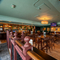 The interior restaurant seating area and bar at The Junction in Upminster, with TVs on the walls, bar stool seating, and an upholstered booth seat along one side of the room. 