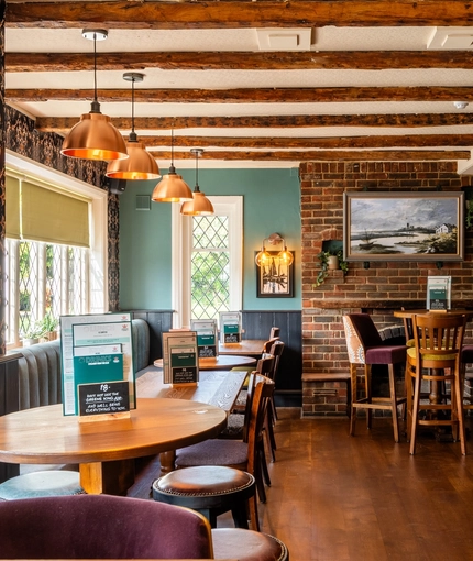 An interior restaurant seating area at The Walkford, with an upholstered booth seat in front of the leaded windows, wooden beams on the ceiling, and a brick fireplace.