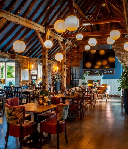 The interior restaurant seating area of The White Hart, with wooden beams, a TV on the wall, and a fireplace.