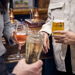 Three people standing at the bar, one of them holding a glass of wine, another holding a glass of Birra Moretti, and the third person holding another drink.