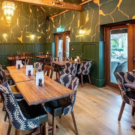 An image of the interior restaurant seating area with partial wooden panelled walls and tables dressed with floral arrangements at The Black Swan.